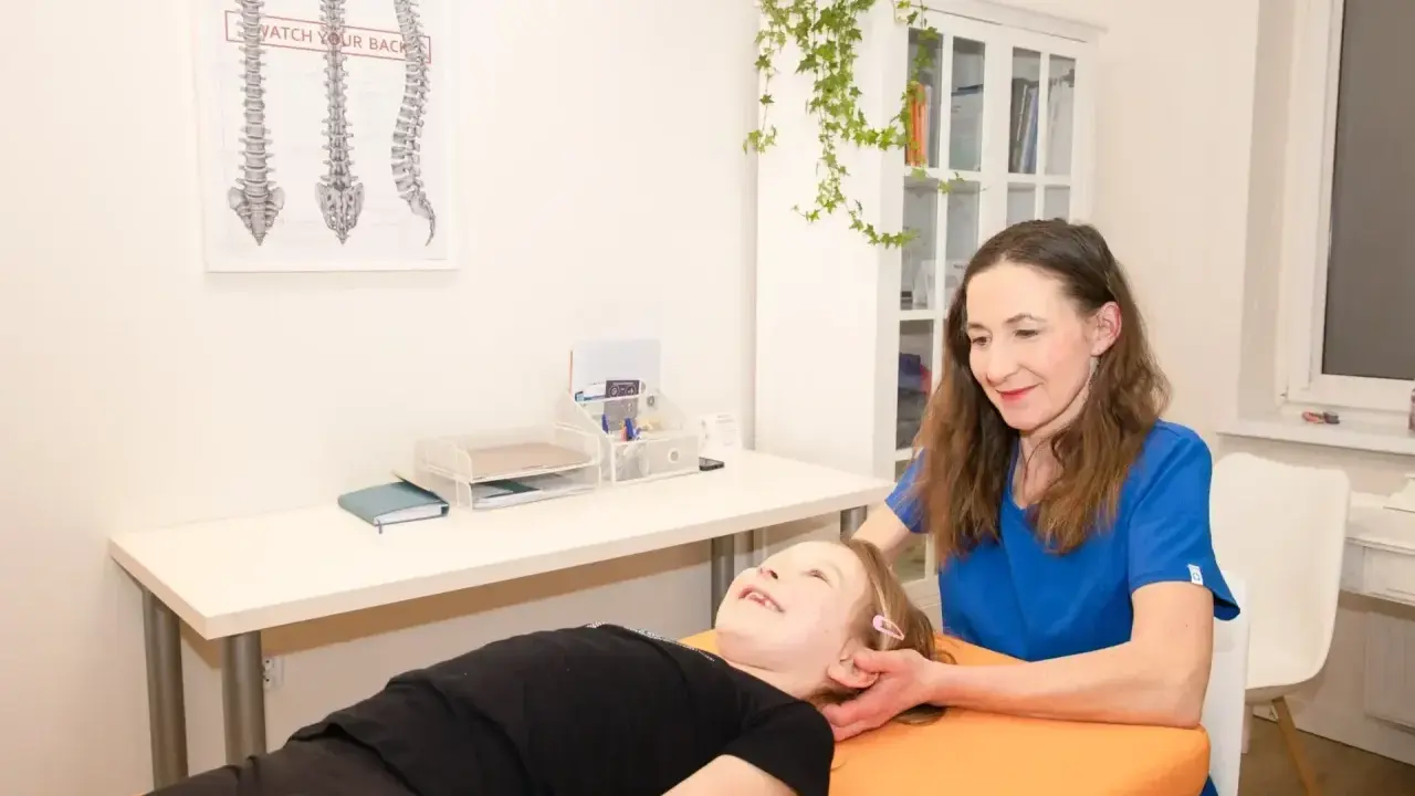 Fizjoterapeutka wykonuje delikatny trening medyczny u uśmiechniętej dziewczynki, która leży na kozetce.