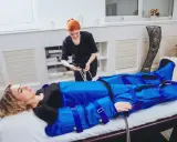 Kobieta w salonie piękności poddawana zabiegowi, który wyjaśnia, co to jest drenaż limfatyczny. Terapeuta przygotowuje urządzenie do masażu uciskowego.