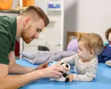 Osteopata dla dzieci delikatnie bawi się z niemowlęciem pluszową pandą, wspierając jego rozwój.