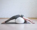 Kobieta wykonuje ćwiczenia na kręgosłup, leżąc na piłce gimnastycznej.