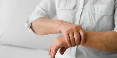 Osoba w białej koszuli masuje nadgarstek, odczuwając ból stawów rąk i nóg.