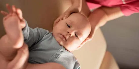 Delikatne dłonie osteopaty pediatrycznego obejmują główkę niemowlęcia, zapewniając mu komfort i wsparcie podczas terapii.