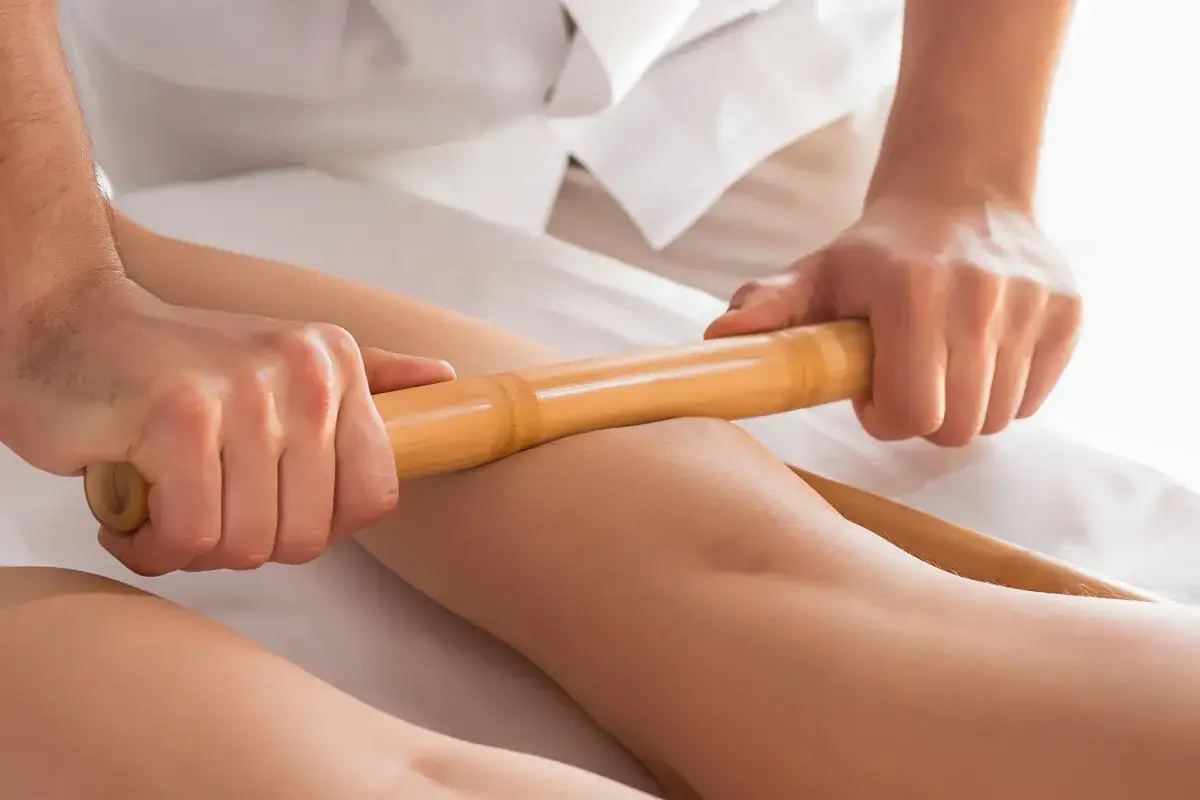 Relaksacyjny masaż pałeczkami bambusowymi na nogach. Terapeuta wykonuje głęboki masaż, który przynosi ulgę i odprężenie.