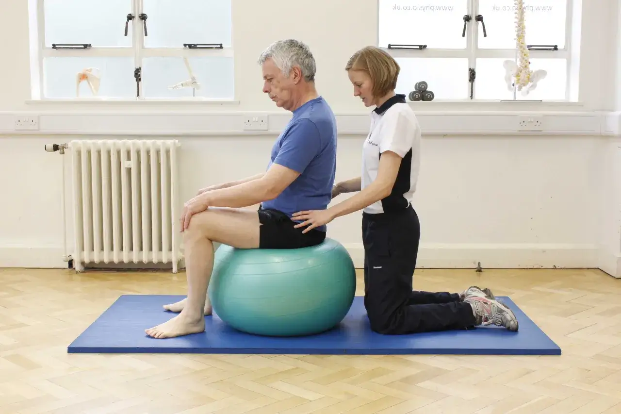 Fizjoterapeuta pomaga pacjentowi w ćwiczeniach propriocepcji na piłce gimnastycznej.