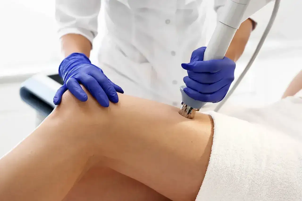 Fizykoterapia laser czas zabiegu: terapeuta w niebieskich rękawiczkach wykonuje zabieg na udzie pacjentki.
