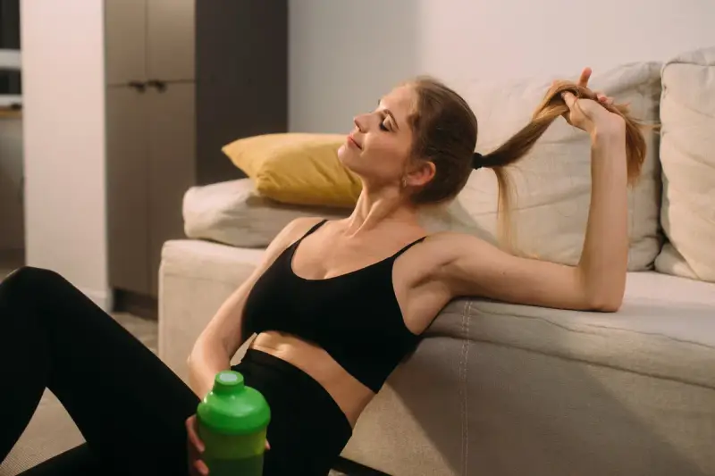 Kobieta w sportowym stroju odpoczywa po treningu, pijąc napój. Czas na regenerację mięśni i relaks.
